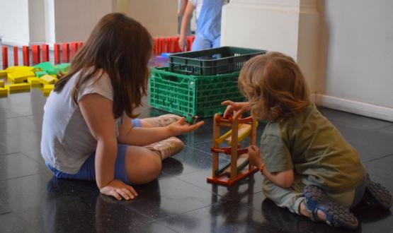 Foto de un niño y una niña de espaldas juegan con maderas sentados en el piso del hall del portal rabú.